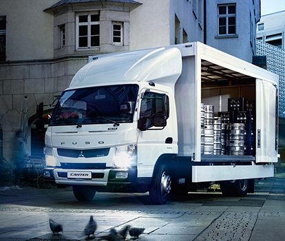 Camion de Carga Canter 915 Fuso Blanco, estacionado alrededores de viviendas donde un trabajador descarga tanques