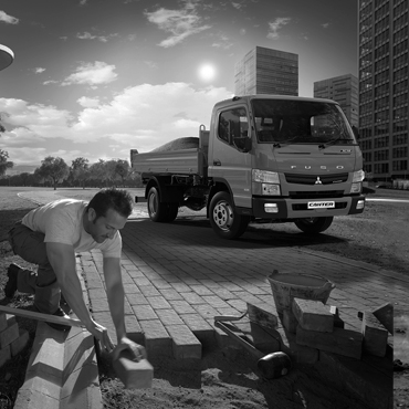 Imagen en Blanco y Negro de un Camion Canter Fuso, situado al costado de un parque interurbano cargando cemento para la construcción de caminos