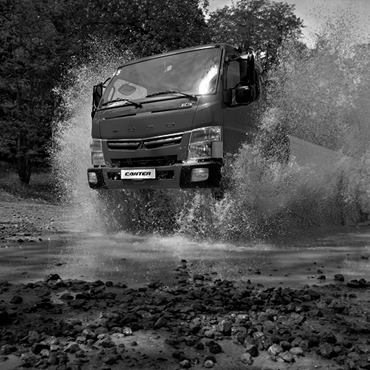 Imagen en Blanco y Negro de un Camion Canter Fuso, cruzando un pequeño rio con piedras, salpicando agua