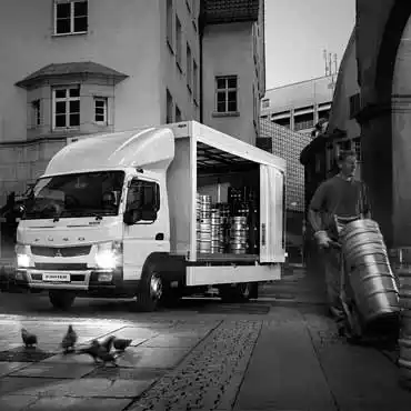 Imagen en Blanco y Negro de un Camion de Carga Canter Fuso, estacionado alrededores de viviendas donde trabajador descarga tanques 