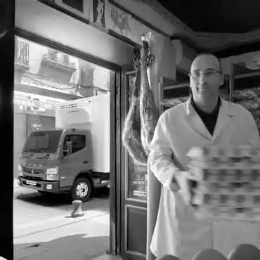 Imagen en Blanco y Nergro, trabajador entregando cajas de huevos a un negocio local, dejando estacionado su camion canter al frende del local