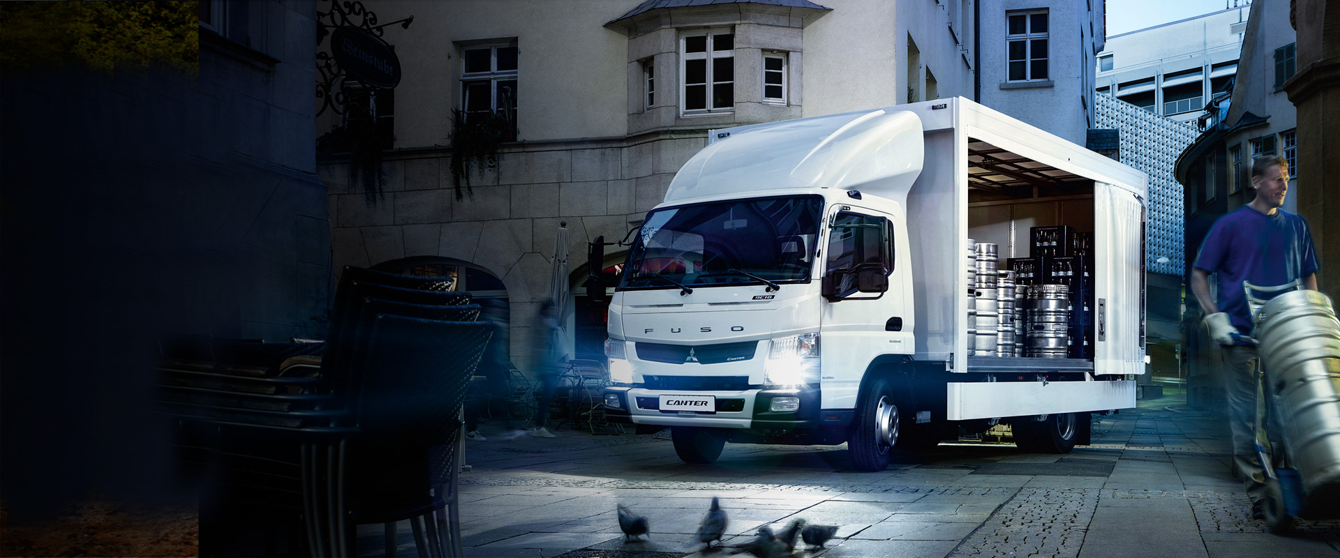 Camion de Carga Canter 915 Fuso Blanco, estacionado alrededores de viviendas donde un trabajador descarga tanques